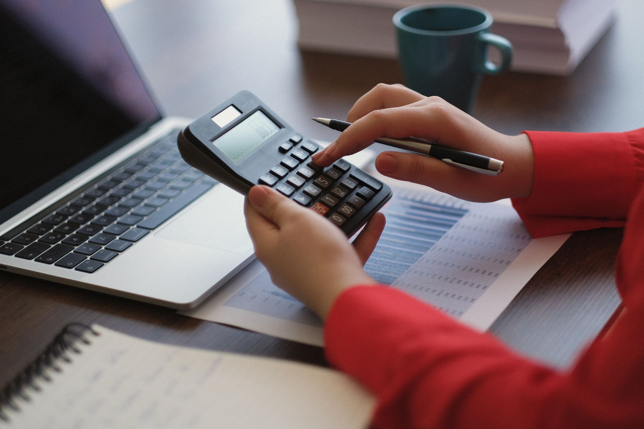 Person calculating budget using calculator and laptop